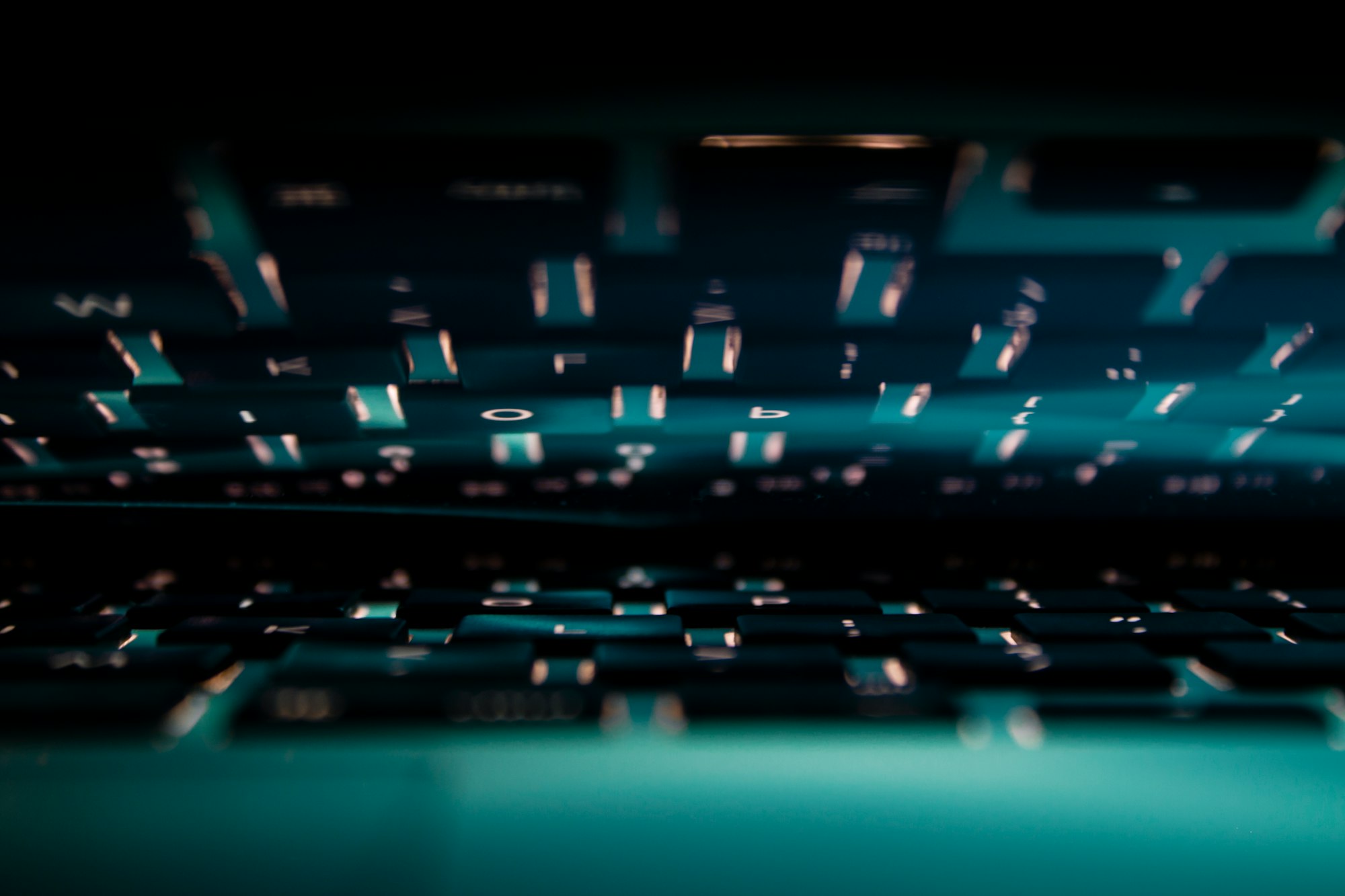 MacBook Pro 2015 reflecting blue cyan light and keyboard keys on the screen.