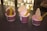 Three cups of ice cream are displayed on a dark countertop. Each cup contains a scoop of ice cream with a waffle biscuit inserted vertically and a yellow spoon resting on the surface. The ice cream flavors appear to include chocolate and strawberry, and the cups are patterned with a red and white design.