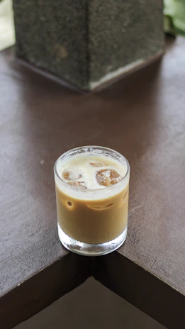 Iced coffee in a glass with condensation, set against a muted terracotta background and a blush napkin.
