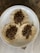 Three small round tortillas topped with a serving of cooked minced meat are arranged on a white ceramic plate. The plate rests on a surface with a dark, marbled texture, and the background includes light-colored wooden flooring.