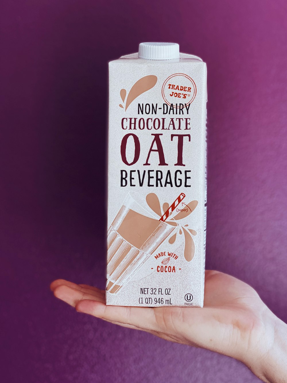 a hand holding a carton of chocolate oat beverage