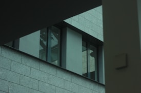A modern building exterior with large glass windows and gray stone tiles. The image captures an architectural detail with clean lines and geometric shapes.