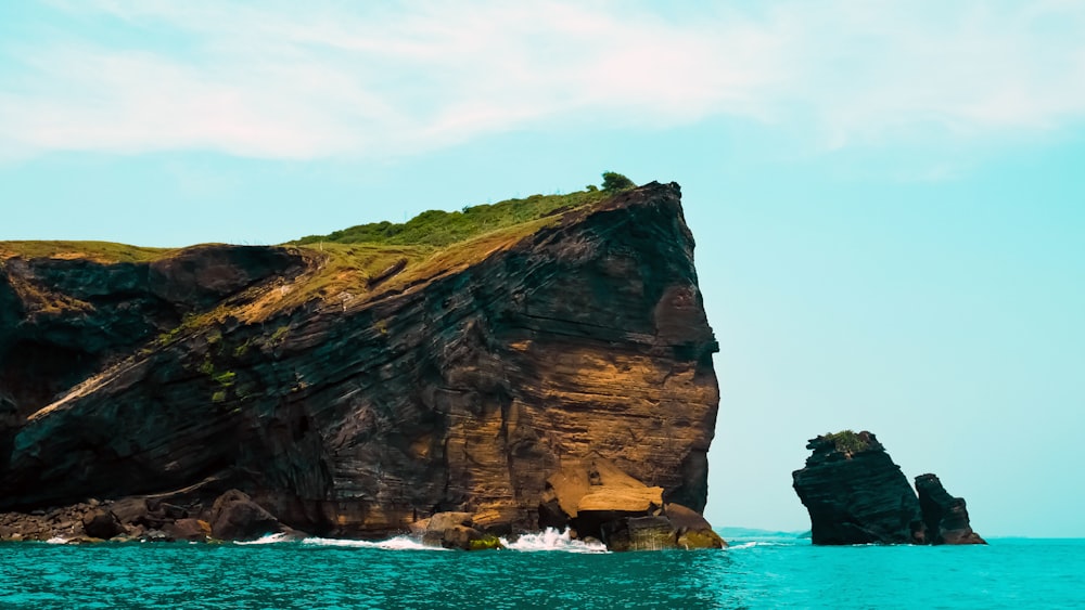 brown and green rock formation on sea under white clouds during daytime