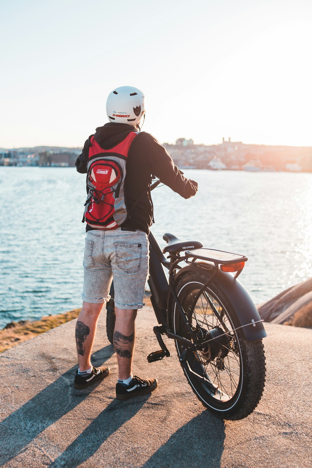 man in red and black jacket and blue denim shorts standing beside black motorcycle during daytime
