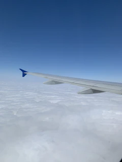An aerial view of a commercial airplane soaring above fluffy white clouds.