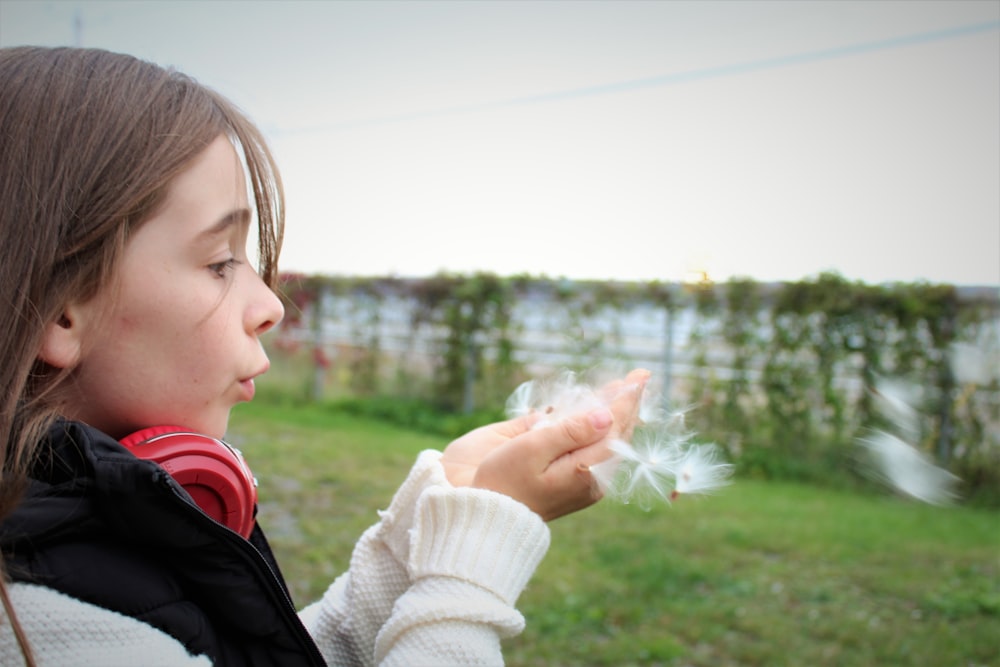 fille en écharpe en tricot blanc tenant une fleur de pissenlit blanc pendant la journée