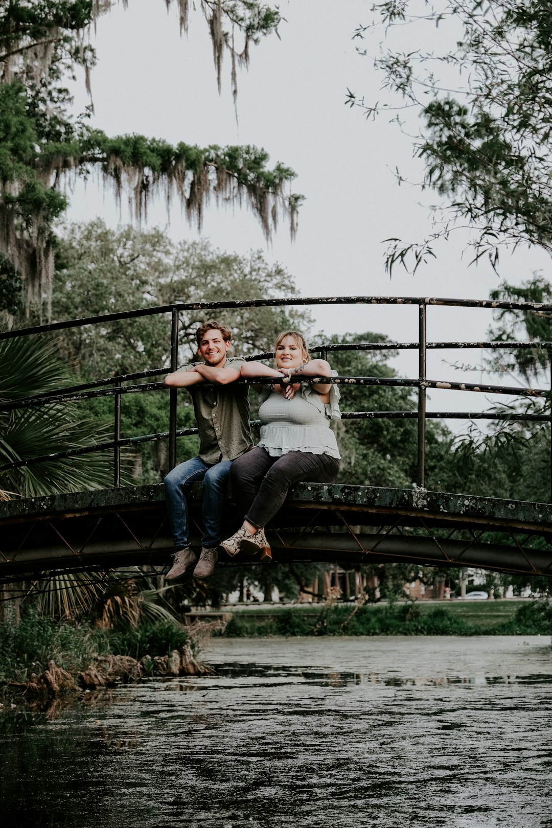 woman in gray shirt and blue denim jeans sitting on black metal fence during daytime