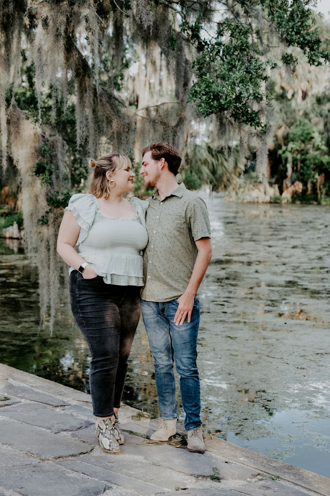 man in gray shirt and woman in white shirt kissing on gray concrete bridge during daytime