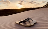 A pair of blue beach sunset flip flops on the sand.