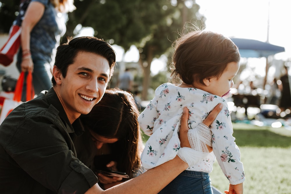 smiling woman in black jacket carrying baby in white and blue onesie