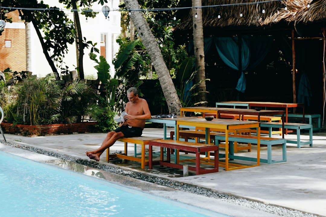 woman in black tank top sitting on brown wooden bench near swimming pool during daytime