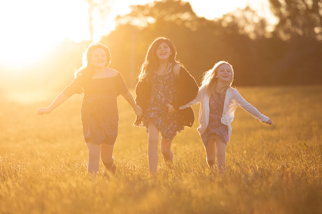Three girls run hand in hand through a sunlit field