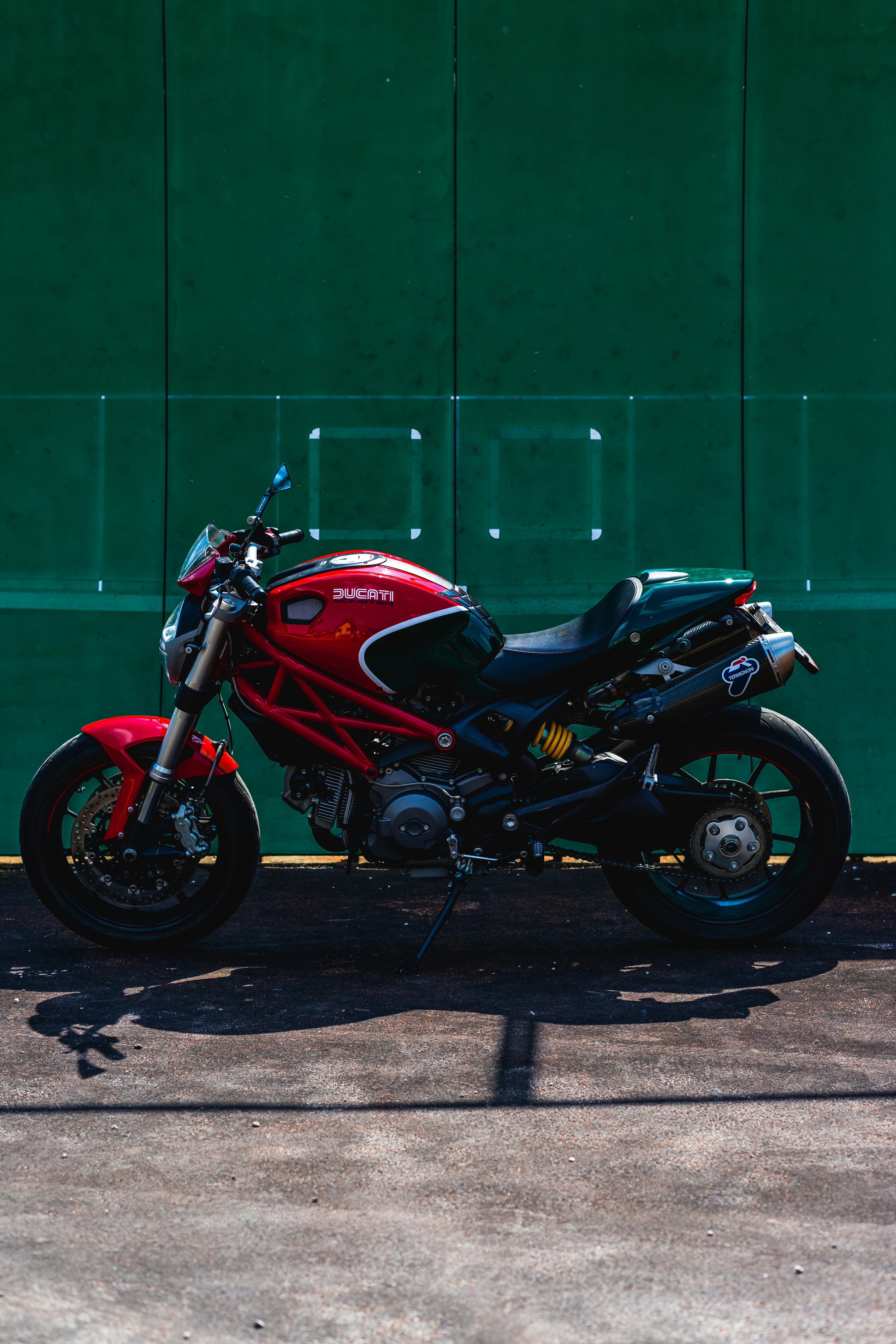 red and black sports bike parked beside green wall