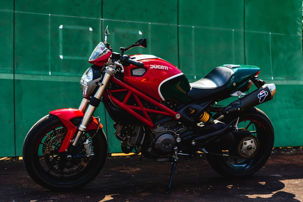 red and black sports bike parked beside green wall