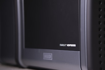 A close-up view of a black and gray electronic device, with the label 'FARGO HDP5000' visible on its surface. The device features a sleek design with rounded edges and some ventilation holes on the side.