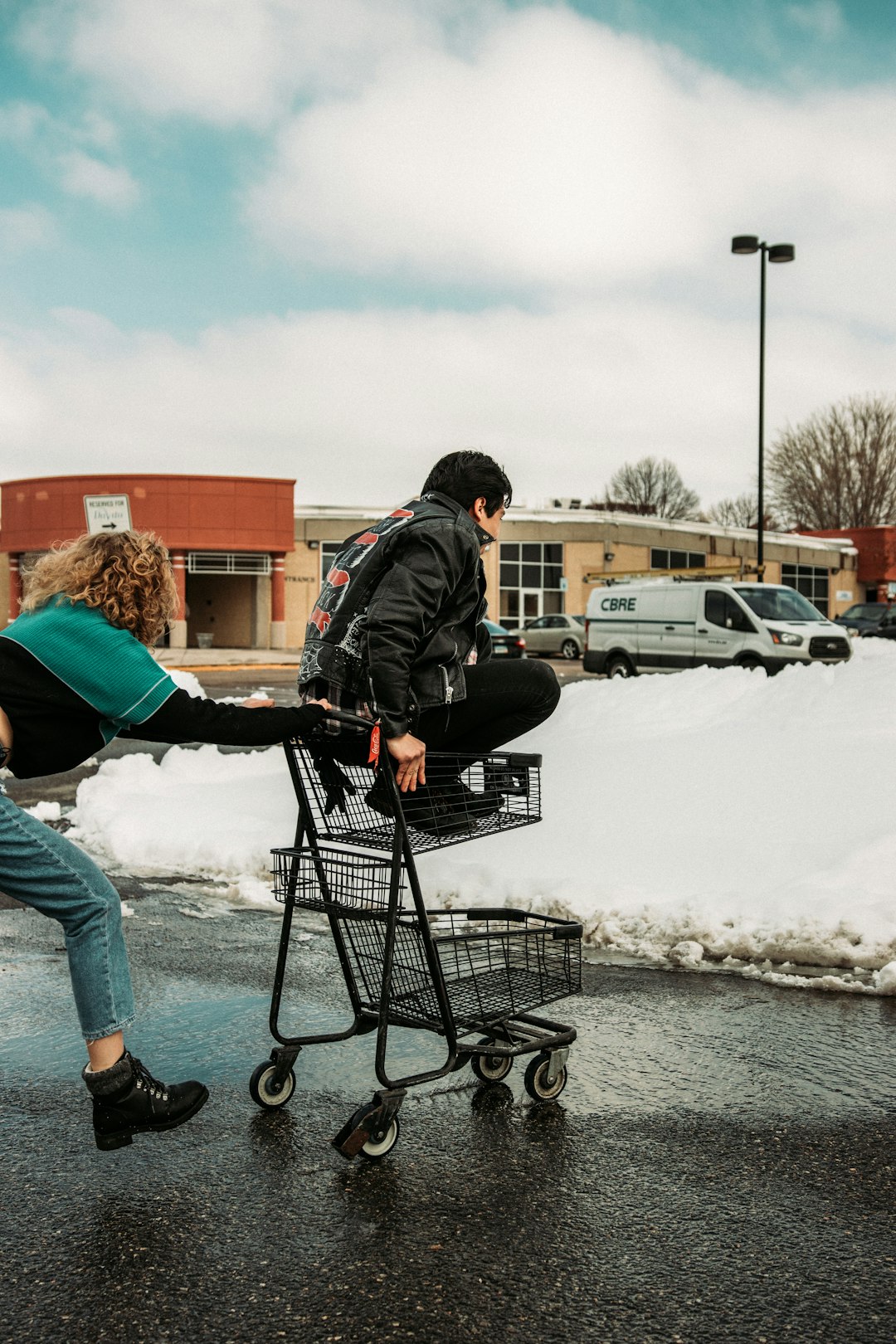 man in black jacket and blue denim jeans riding on black shopping cart on snow covered