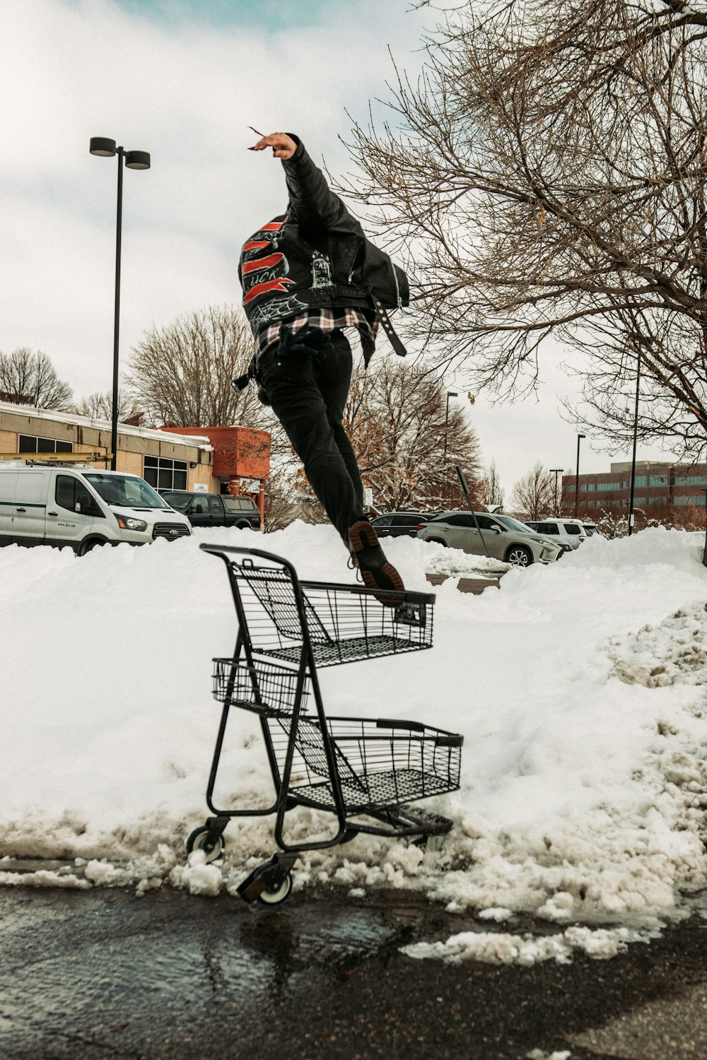 man in black jacket and brown pants riding on black shopping cart on snow covered ground