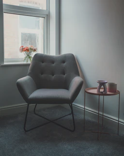 A cozy corner with a plush ivory armchair, a stack of fashion magazines, and a vase of fresh flowers on a side table.