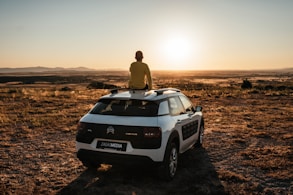 man in brown jacket sitting on white jeep wrangler on brown field during daytime