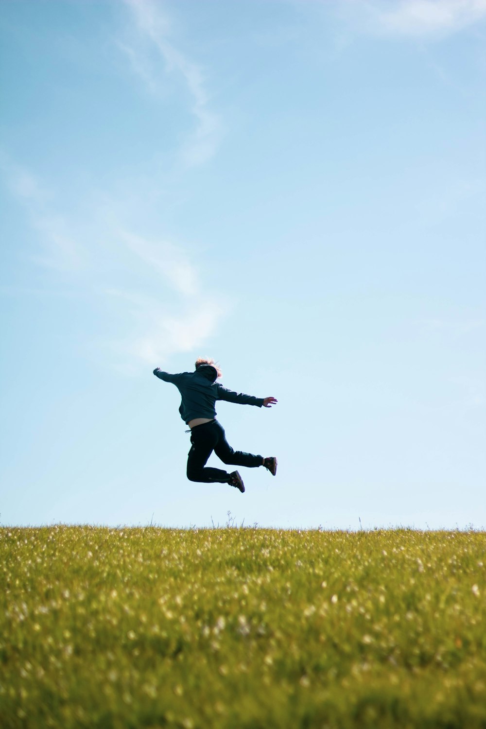 man in black jacket jumping on green grass field during daytime