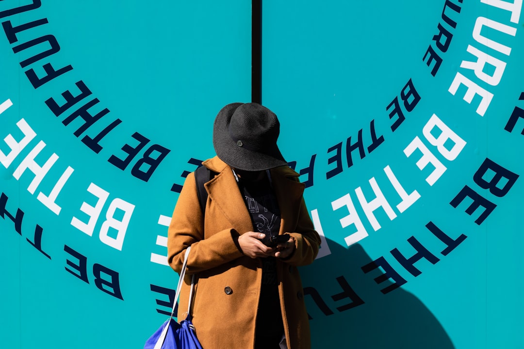 man in brown coat wearing black fedora hat standing beside blue and white wall