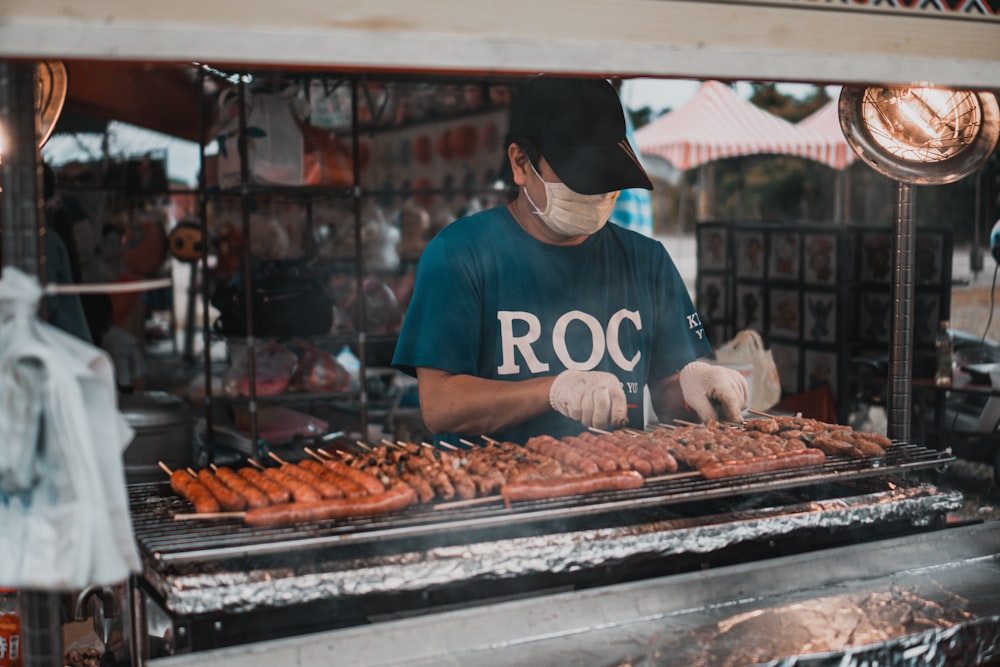 Hombre con camiseta roja de cuello redondo y gorra negra de pie frente a la carne