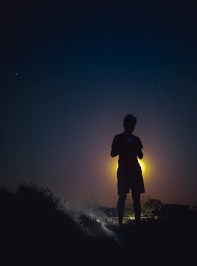 A mysterious silhouette standing before a glowing portal of light at twilight.
