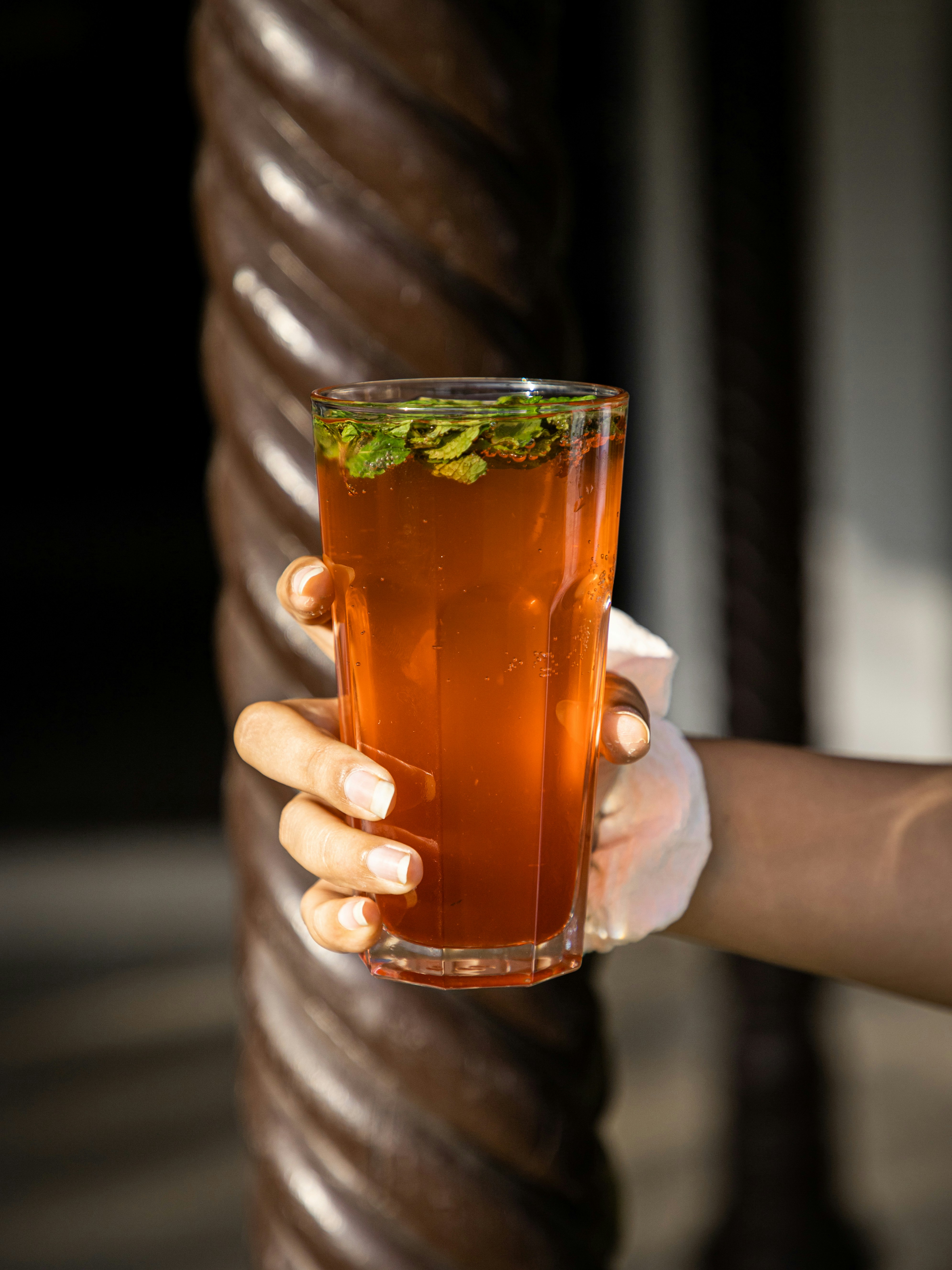 person holding clear drinking glass with brown liquid