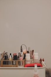 Assorted cosmetic and skincare items are organized neatly in a container. Various bottles, tubes, brushes, and other beauty tools like a curling iron are visible.