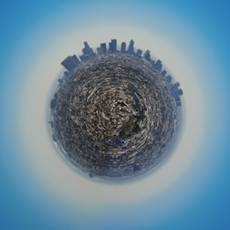 A panoramic view of a city presented in a circular, spherical format, giving the impression that the cityscape is encapsulated on a small planet. Tall skyscrapers are prominently visible around the edge, while smaller buildings and streets fill the interior.