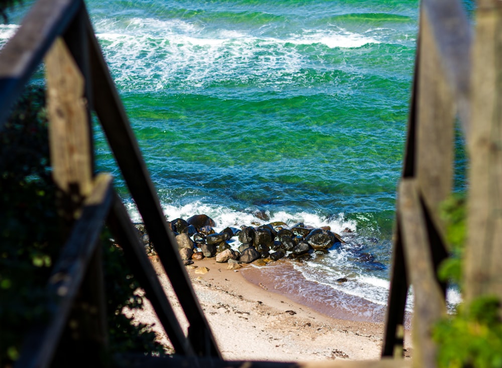 brown wooden railings near sea waves crashing on shore during daytime