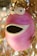 A whimsical ceramic sculpture with a round, pink body and a wide open mouth resembling a surprised expression. The eyes are large and cartoonish, positioned on top of the head, contributing to the playful appearance. Dried twigs or vines are attached to the top, adding an organic touch to the otherwise smooth surface of the sculpture.