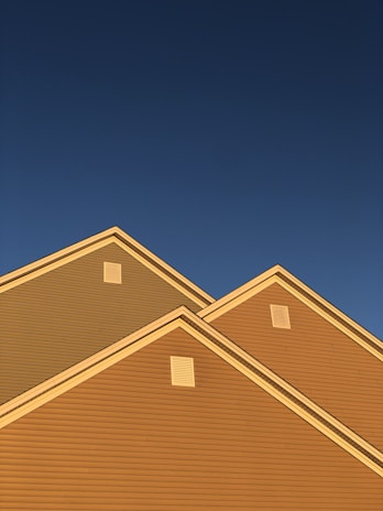 A series of house rooftops illuminated by golden sunlight against a backdrop of clear deep blue sky. The triangular roof peaks are prominent, showcasing the distinct lines and ventilation panels.