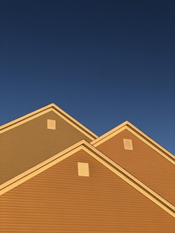 A series of house rooftops illuminated by golden sunlight against a backdrop of clear deep blue sky. The triangular roof peaks are prominent, showcasing the distinct lines and ventilation panels.