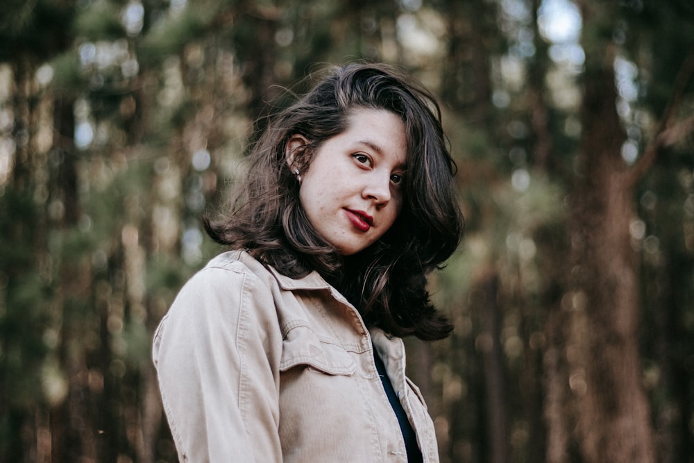 woman in brown jacket standing near trees during daytime