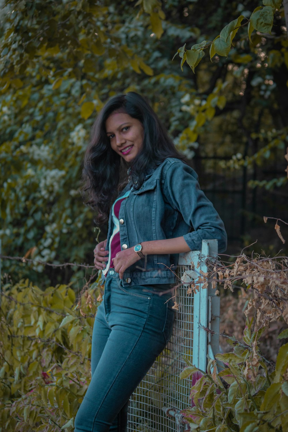 woman in blue denim jacket and blue denim jeans standing beside gray metal fence during daytime