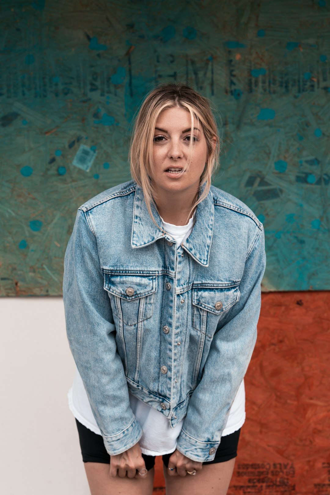 woman in blue denim jacket standing near blue and brown wall