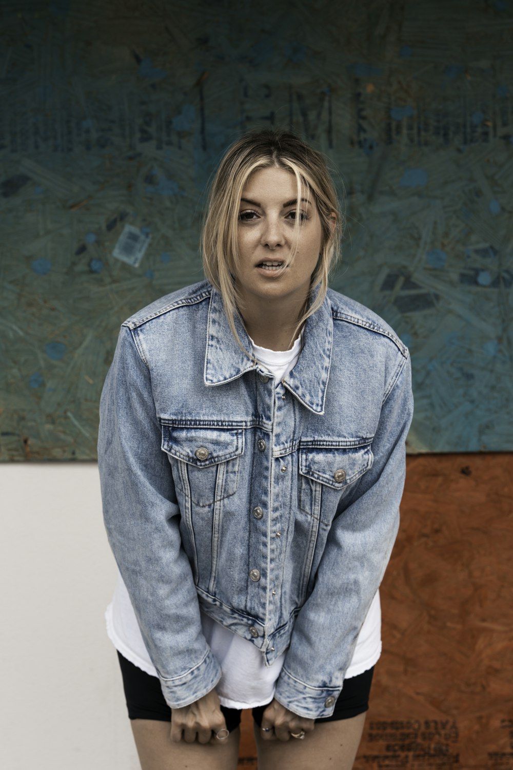 woman in blue denim jacket standing near blue and brown wall