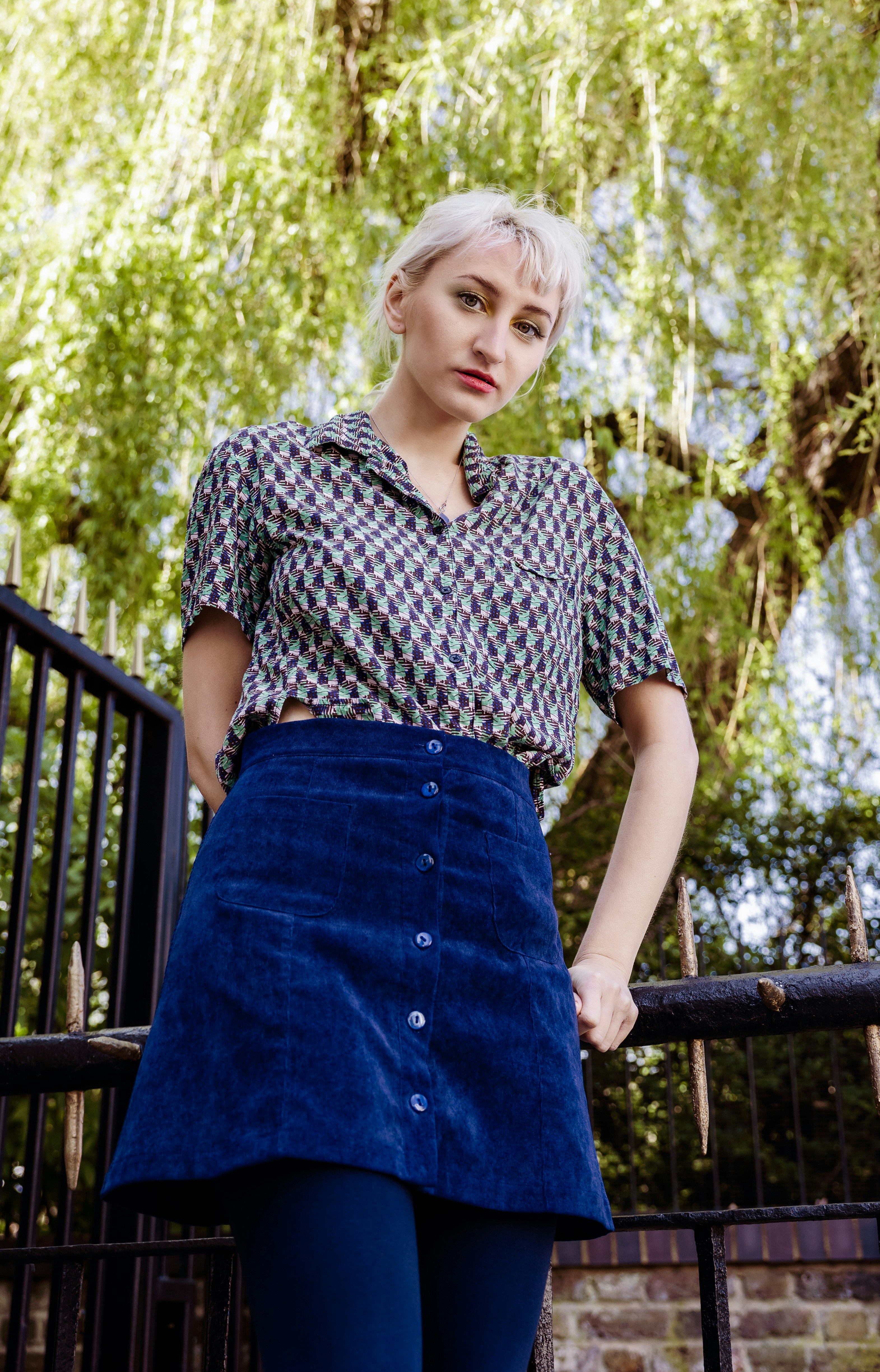 woman in black and white floral shirt and blue skirt standing near brown wooden fence during