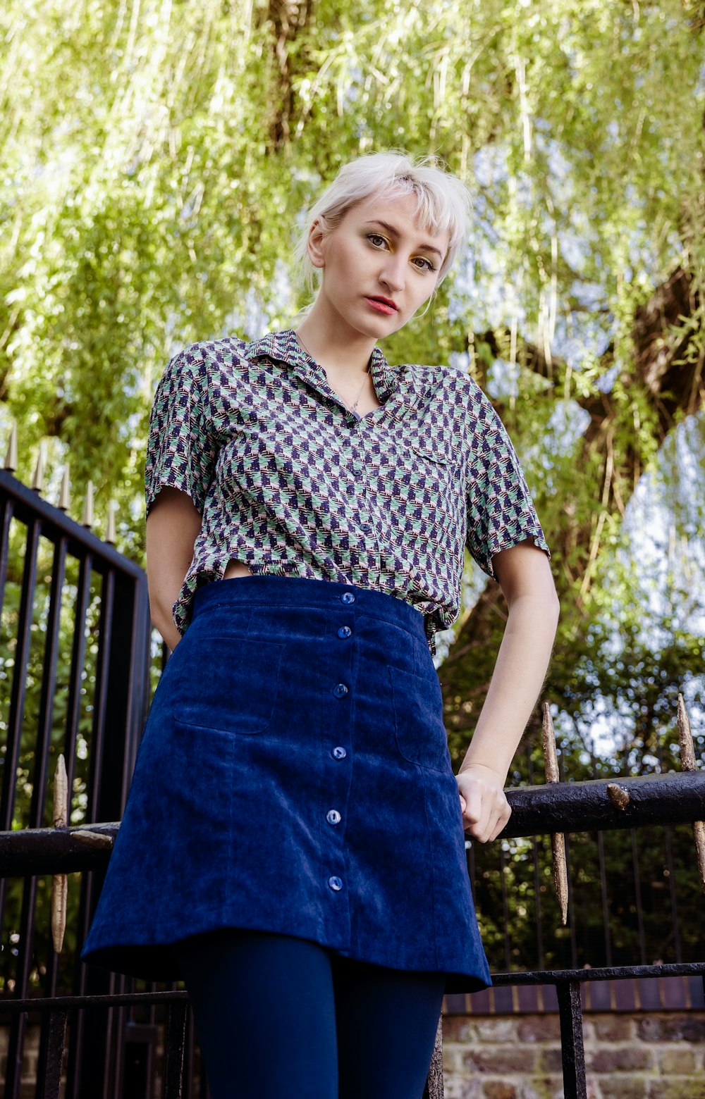 woman in black and white floral shirt and blue skirt standing near brown wooden fence during