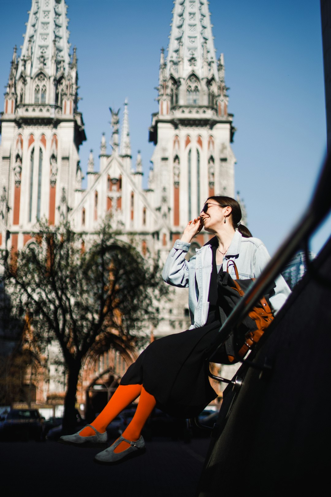 woman in white coat and orange pants sitting on black metal railings during daytime