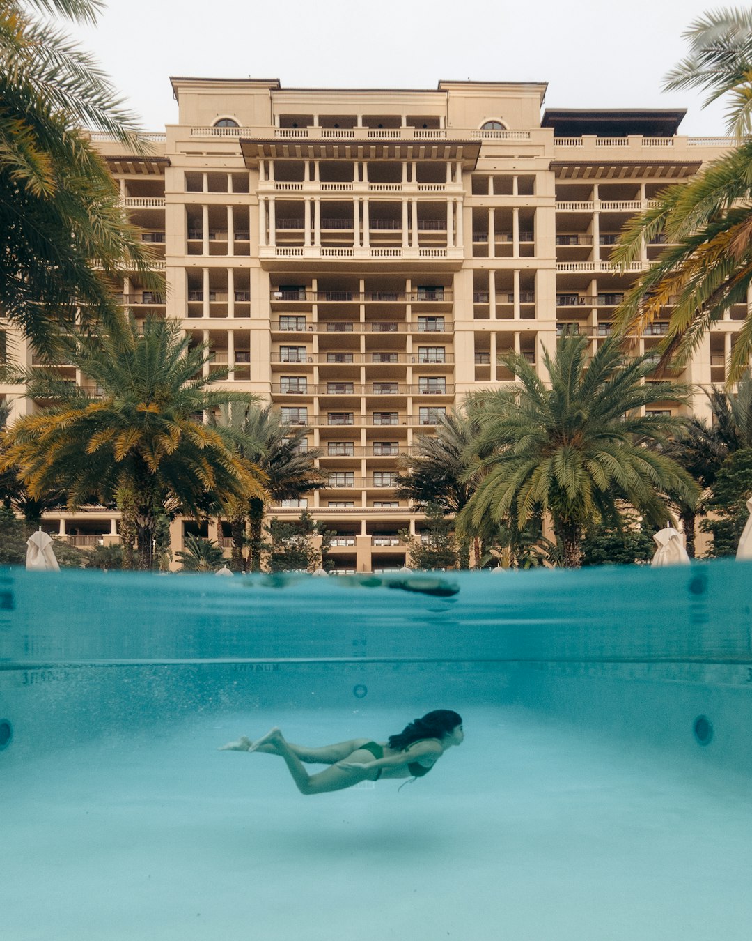 man in swimming pool near palm trees and building during daytime