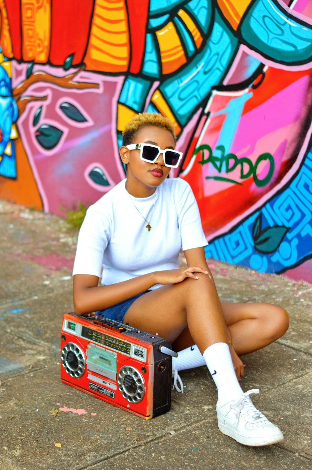 Femme en t-shirt à col rond blanc et short en jean bleu assise sur un sol en béton