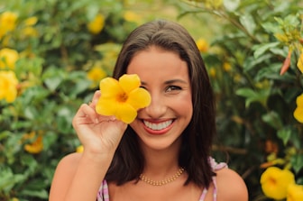 woman in white and purple tank top holding yellow flower