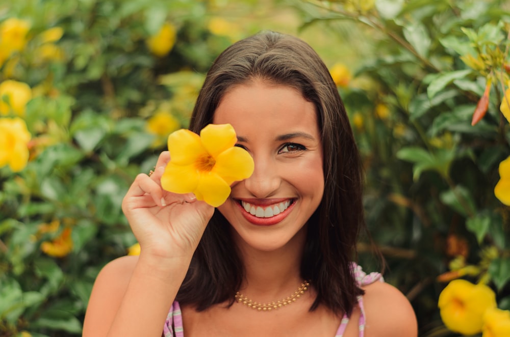 woman in white and purple tank top holding yellow flower