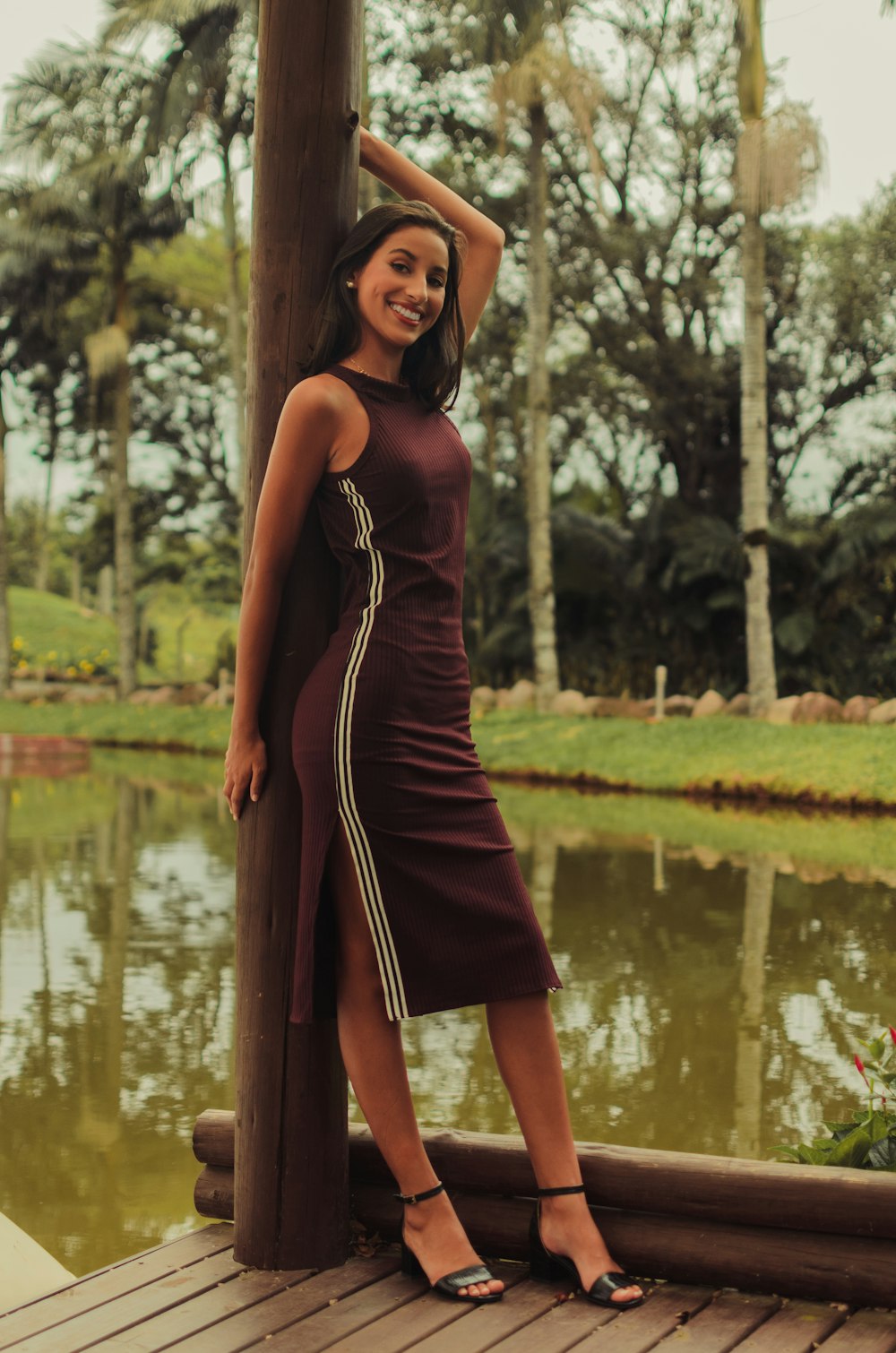 woman in red sleeveless dress standing beside brown wooden post during daytime