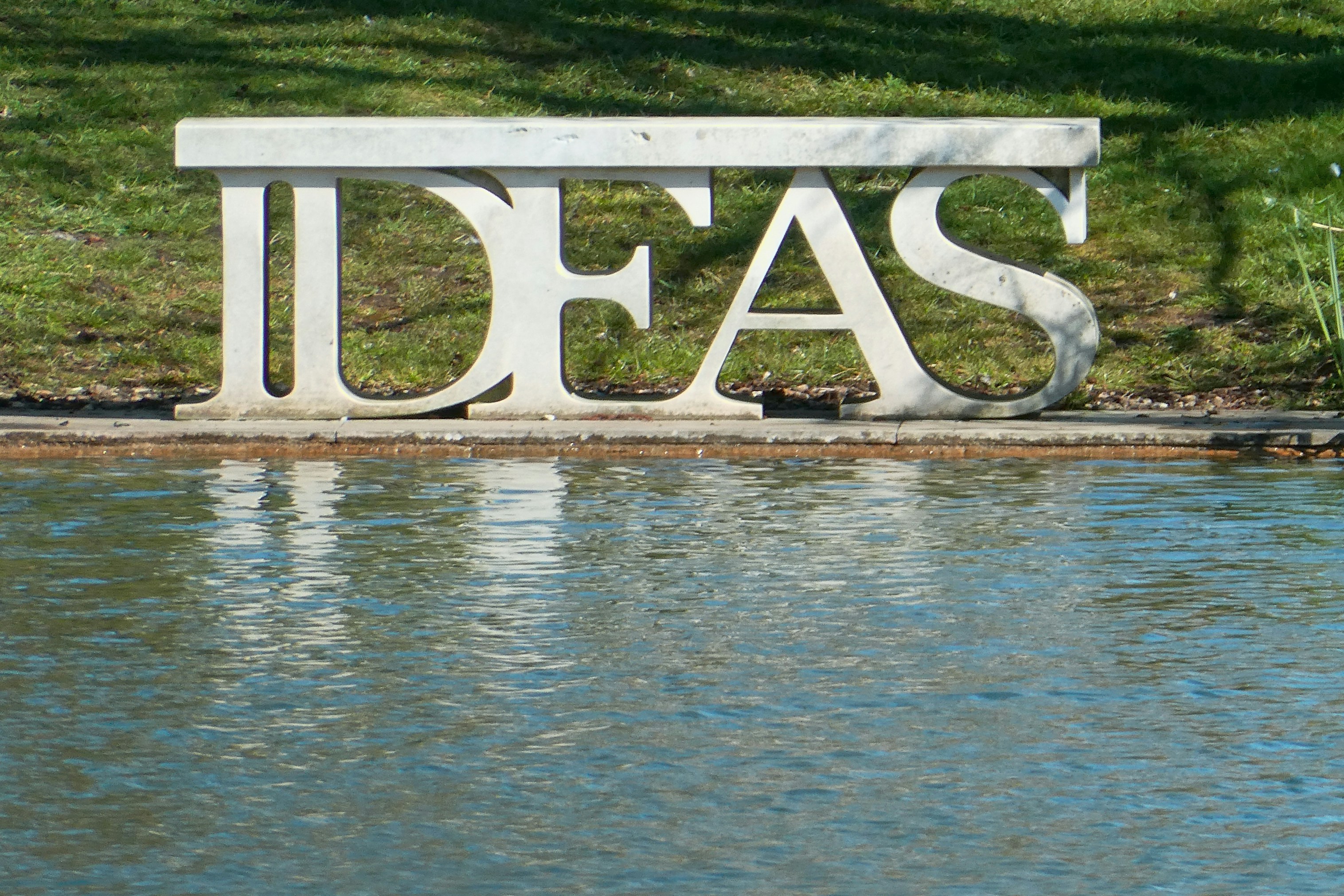 A seat in the shape of the word ideas, reflected in the water of a lake.