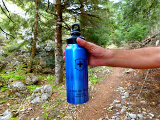 A runner happily holding clarivita while crossing a scenic outdoor trail.