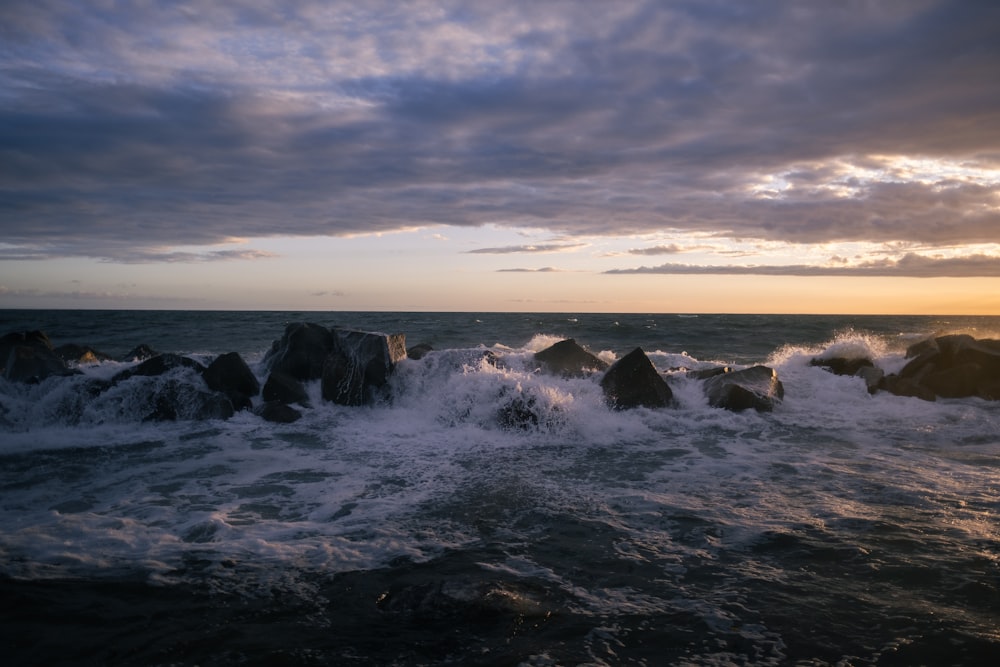 ocean waves crashing on rocks under cloudy sky during daytime