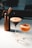 On a white marble countertop, there is a tall copper-colored cream whipper next to a martini glass filled with a creamy espresso cocktail. Beside it is another cocktail in a coupe glass, topped with a halved passion fruit. In the foreground, there is a small shot glass filled with a clear liquid.